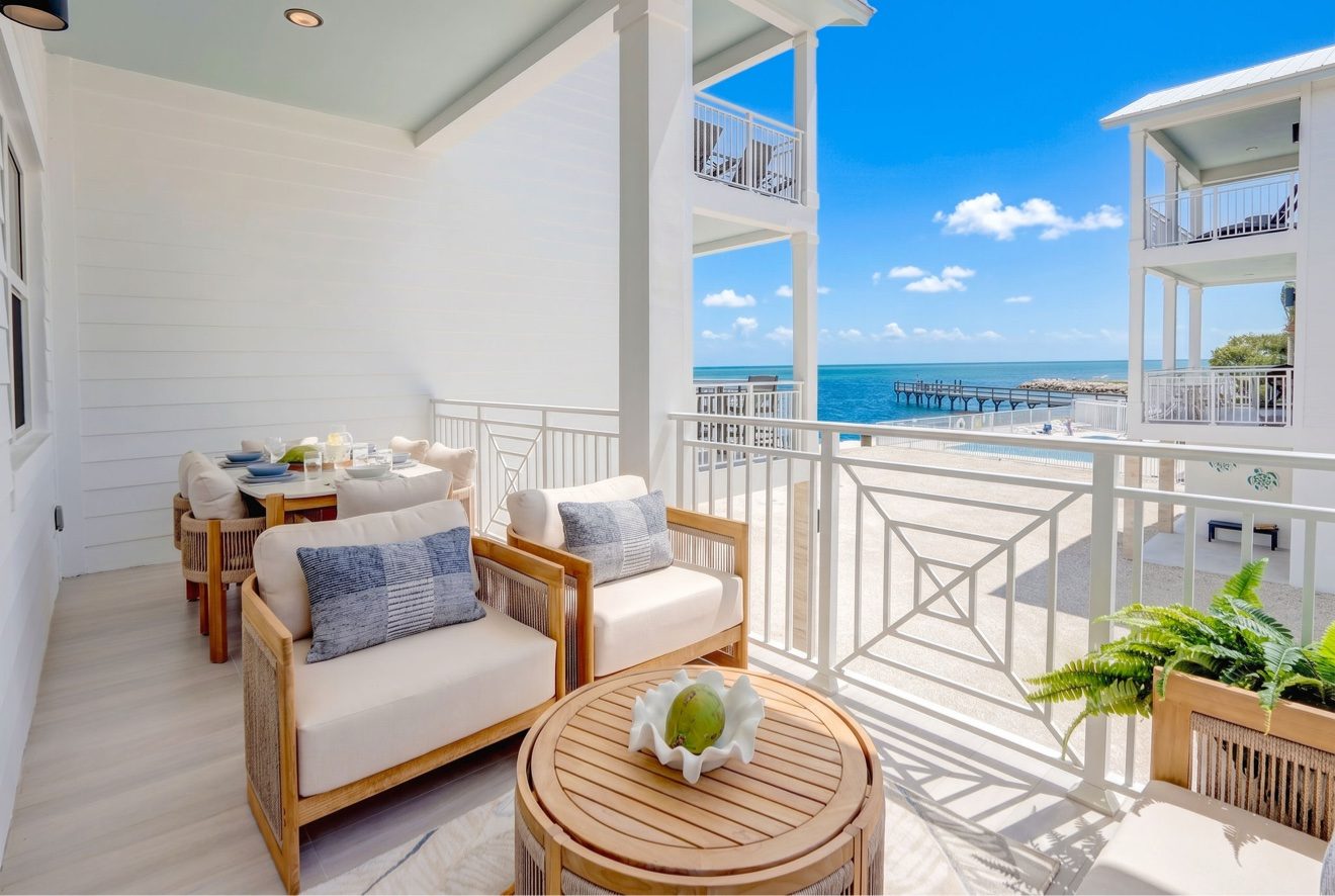 Balcony dining area with table and chairs facing the ocean and community dock